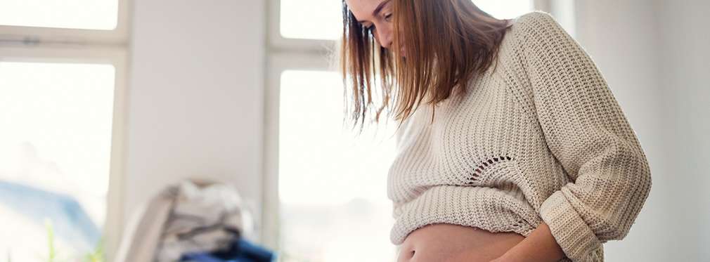 Изображение на бременна жена, която се опитва да си обуе вече омалели дънки