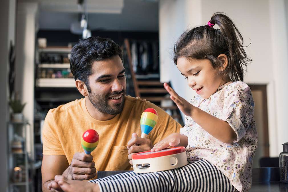 Изображение на момиченце и баща му, които се забавляват с музикални инструменти и грачки