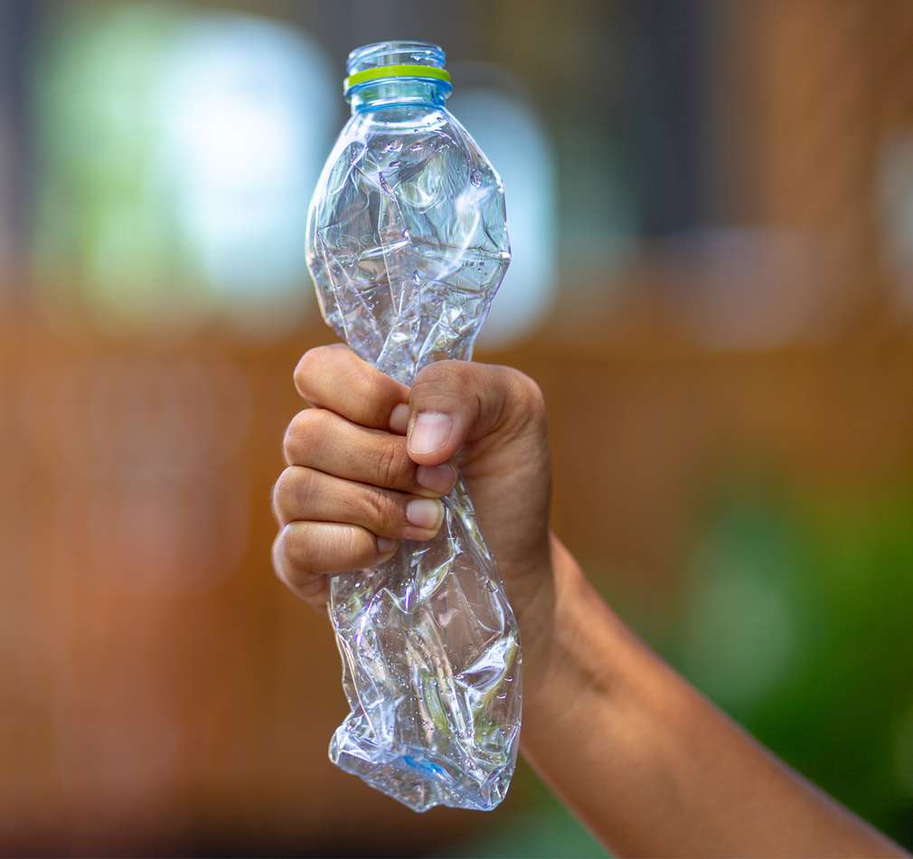 Изображение на протегната човешка ръка със смачкана пластмасова бутилка в дланта