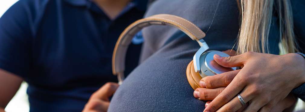 Изображение на корем бременна жена, на който са поставени слушалки