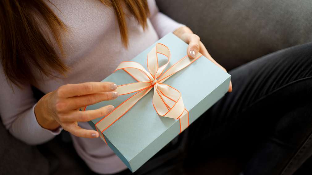 Frau sitzt auf Sofa und hält ein blau verpacktes Geschenk in der Hand