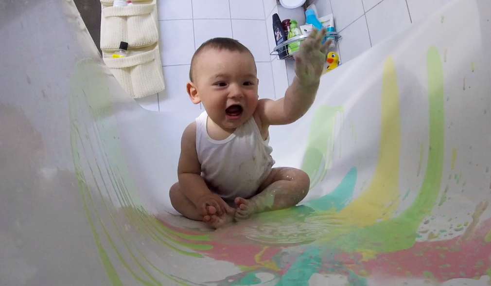 Baby sitzt in der Badewanne und spielt mit essbarer Farbe Baby sitzt in der Badewanne und spielt mit essbarer Farbe