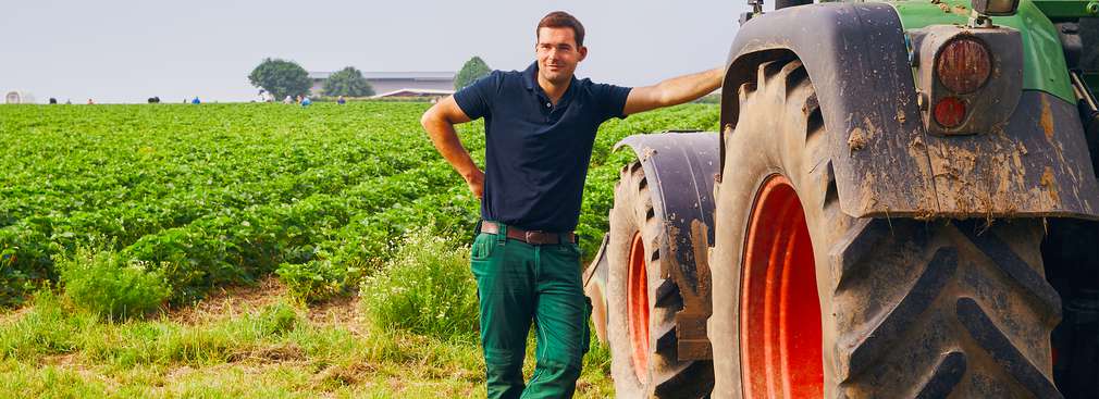Bauer lehnt an Traktor auf einem Feld