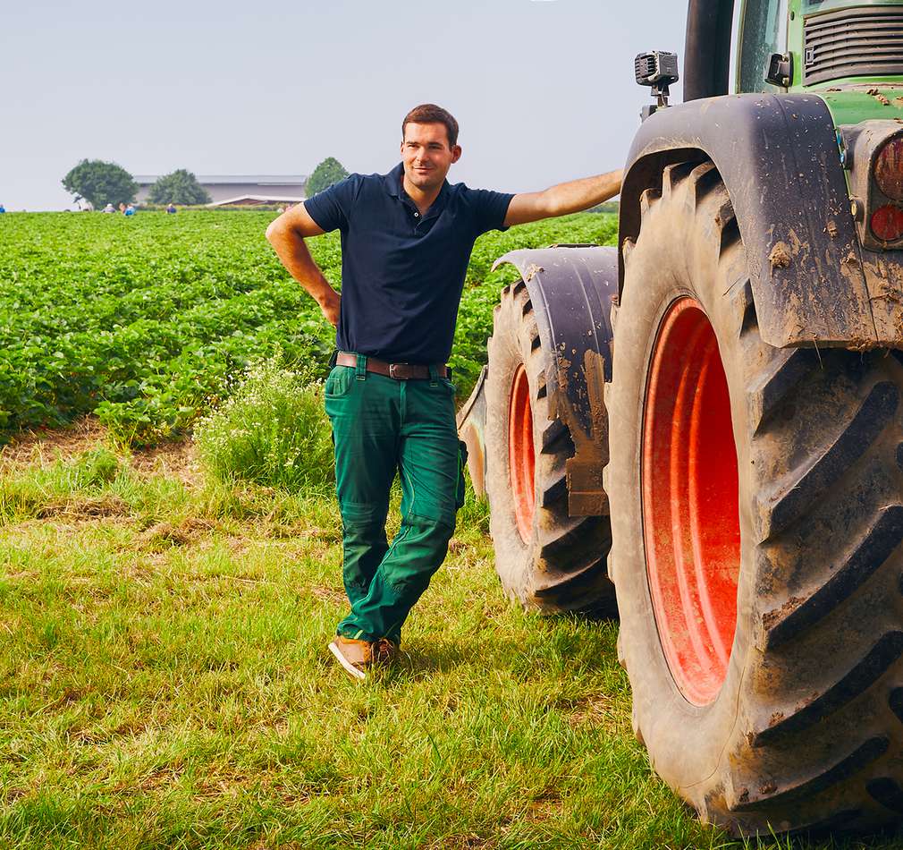 Bauer lehnt sich an Traktor auf einem Feld Bauer lehnt sich an Traktor auf einem Feld