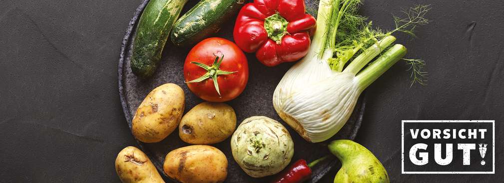 Teller mit Kartoffeln, Tomate, Paprika, Fenchel, Gurken, Kohlrabi und Birne; Schriftzug: Vorsicht gut!