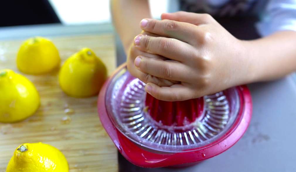 Kind presst mithilfe einer Zitronenpresse frische Zitronen aus Kind presst mithilfe einer Zitronenpresse frische Zitronen aus