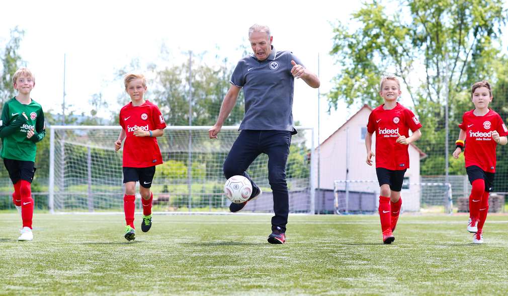 Kinder laufen auf dem Fußballplatz neben Fußballspieler Charly Körbel Kinder laufen auf dem Fußballplatz neben Fußballspieler Charly Körbel