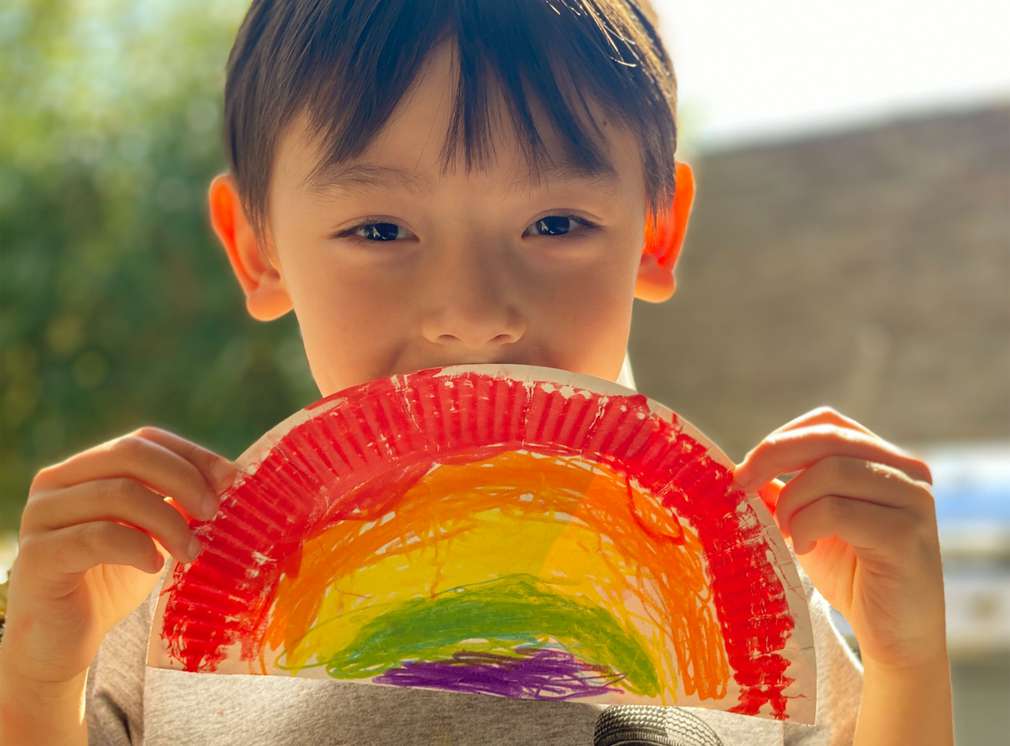 Junge hält einen aus Pappe, Schnipsel und Buntstiften gebastelten Regenbogen Junge hält einen aus Pappe, Schnipsel und Buntstiften gebastelten Regenbogen