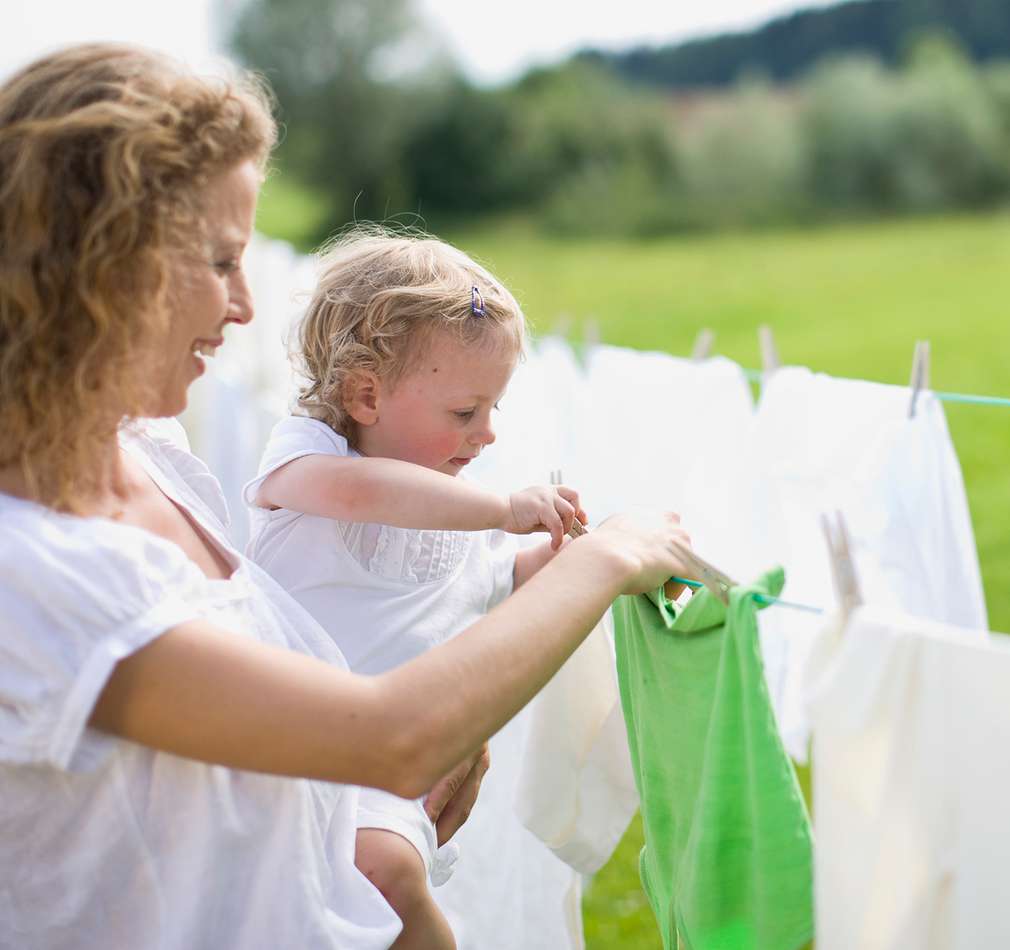 Изображение на майка с малко дете на ръце, заедно слагат щипки на прането на простора