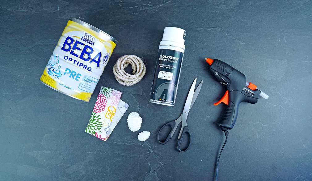 Dose Nestlé BEBA Pre- oder Folgenahrung, weißer Acryl-Sprühlack, Dekostoffband, Kordel, Schere, Heißklebepistole, und Muscheln Dose Nestlé BEBA Pre- oder Folgenahrung, weißer Acryl-Sprühlack, Dekostoffband, Kordel, Schere, Heißklebepistole, und Muscheln