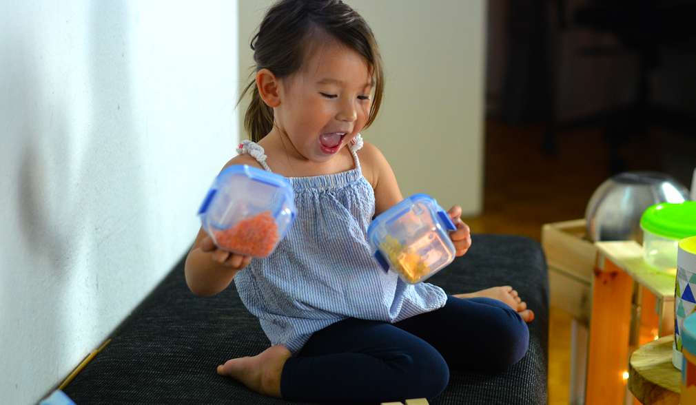 Kleines Mädchen schüttelt zwei Plastikdosen mit Inhalt Kleines Mädchen schüttelt zwei Plastikdosen mit Inhalt