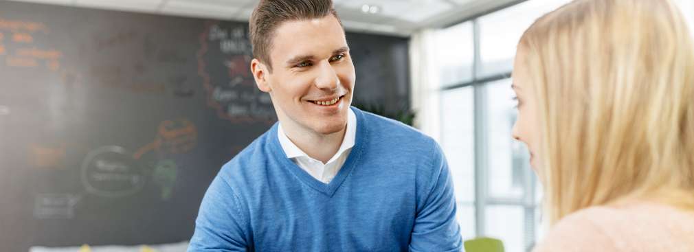 Zwei Trainees besprechen am Hochtisch im Ideenraum vor einem Laptop eine Präsentation. 