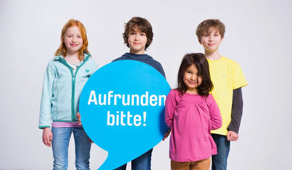 Haben Sie auch schon aufgerundet? Kind hält Sprechblase mit Aufschrift "Aufrunden bitte!"